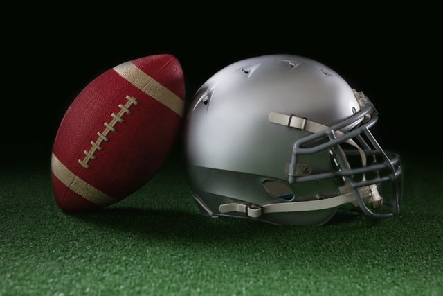 American football leaning on headgear against black background