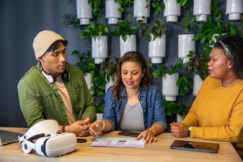 Diverse team collaborating over design mockups with vr headset in modern green workspace