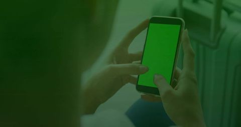 Traveler holding smartphone with green screen next to suitcase