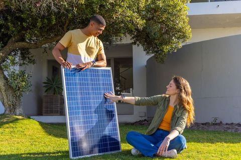 Diverse friends installing solar panel in front yard of contemporary home for clean energy