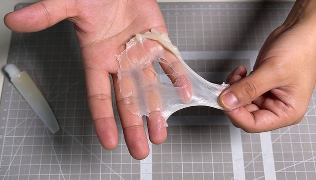 Hands pulling translucent sticky slime stretching across palm on craft cutting mat macro