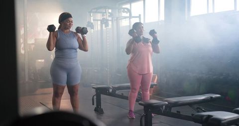 Plus-size women lifting dumbbells together in gym wearing blue and pink activewear