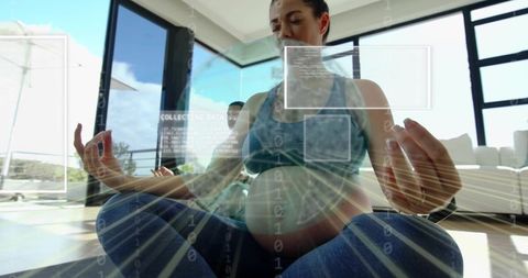 Pregnant woman meditating at home with digital health overlay and sunlight-filled modern space