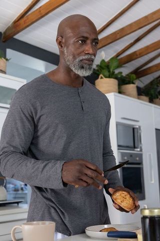 Mature african man in grey henley slicing bread roll at modern kitchen counter