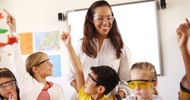 Female teacher engaging students in classroom science activity. All wearing safety glasses, suggesting focus on hands-on experiments, possibly related to STEM education. Ideal for illustrating educational settings, science learning, or promoting science programs for young students.