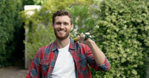 Cheerful Young Man Enjoying Gardening in a Lush Backyard