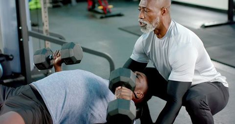 African american trainer spotting man pressing dumbbells on bench for strength building