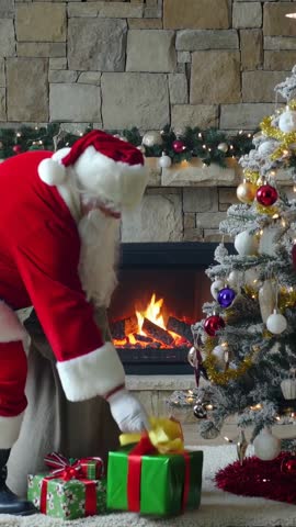 Santa placing gifts from burlap sack under Christmas tree by cozy fireplace | Vertical video