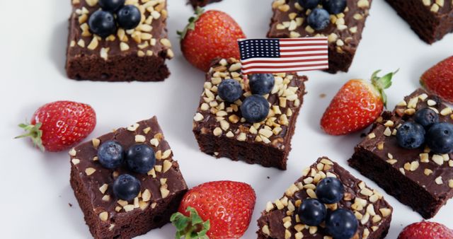 Slices of chocolate brownies topped with fresh blueberries and strawberries are arranged neatly, with an American flag adding a patriotic touch, with copy space. Perfect for a Fourth of July celebration, these treats combine indulgence with a nod to national pride.