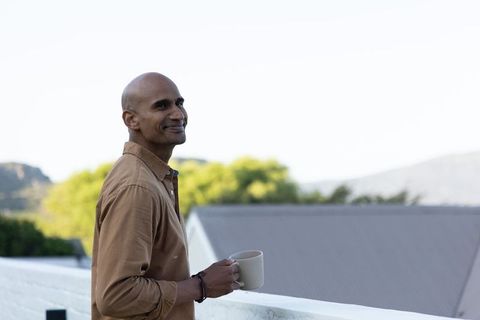 Bald middle-aged man standing on balcony holding ceramic mug enjoying quiet morning