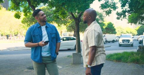 Diverse friends chatting on urban sidewalk holding smartphone and wearing wristwatch