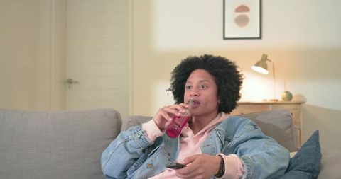 Mid-adult african-american man relaxing on couch drinking red beverage and watching tv remote