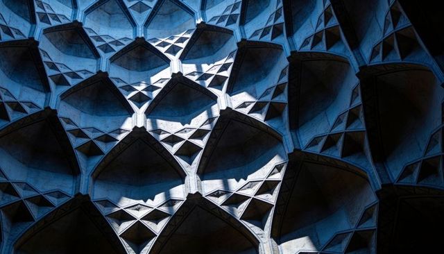 Blue-lit concrete honeycomb vaults creating repeating pointed arches and geometric rhythm