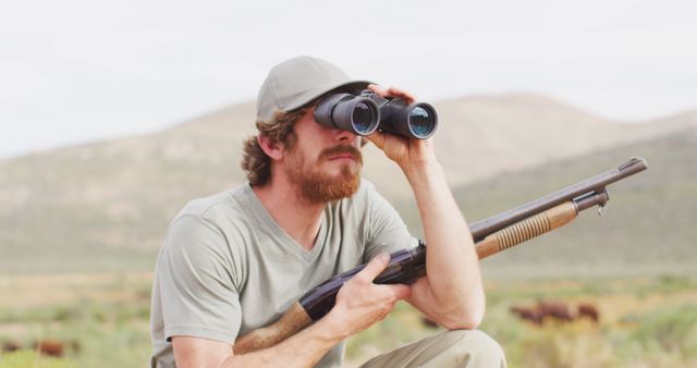 Bearded caucasian male survivalist holding hunting rifle looking using binoculars in wilderness. exploration, travel and adventure, survivalist in nature.