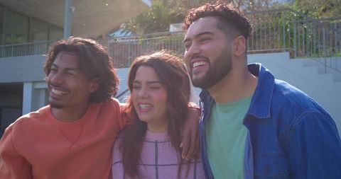 Friends laughing and embracing on sunlit terrace stairs for campus lifestyle and community