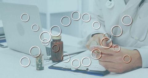 Physician reviewing prescription bottle, patient notes, using laptop in medical office