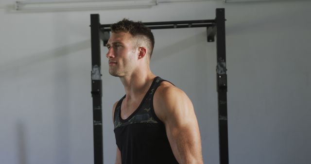 Young athletic man wearing a tank top preparing for workout in gym. Ideal for fitness blog content, gym promotions, exercise tutorials, and wellness motivation materials.