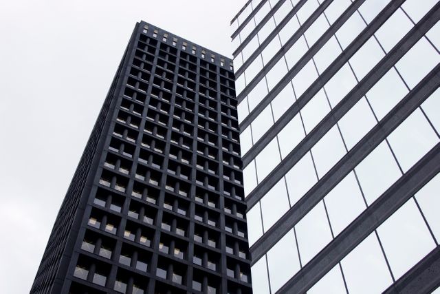 This image captures tall, modern skyscrapers in an urban environment under a cloudy sky. These towering buildings with their grid-like windows reflect contemporary architectural design, perfect for articles, websites, or presentations focused on business, finance, real estate, or urban development.
