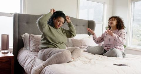 African American friends sitting on bed chatting and adjusting hair in cozy loungewear