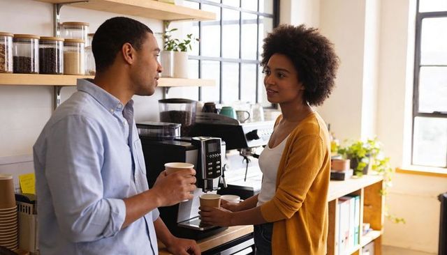 Coworkers sharing coffee break conversing in bright office kitchen with espresso machine