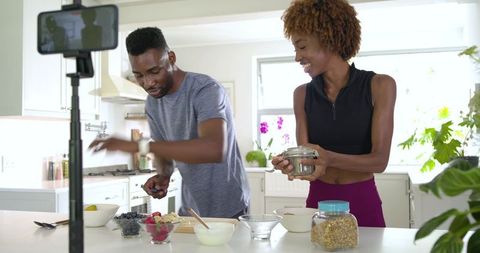 Black couple preparing healthy breakfast while recording content in bright modern kitchen