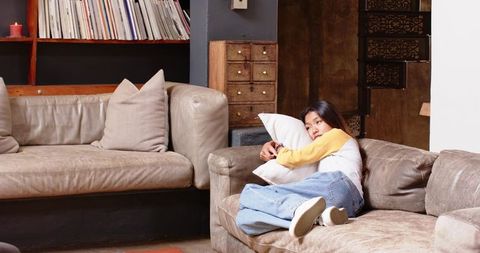 Asian Woman Hugging Pillow Relaxing in Cozy Living Room with Leather Sofa