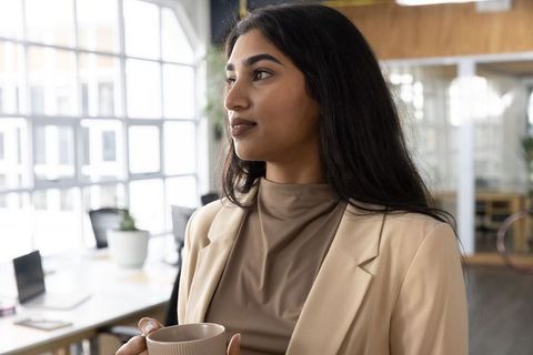 Confident indian professional holding mug in sunlit modern coworking office