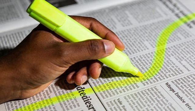 Dark-skinned Hand Highlighting Newspaper with Neon Yellow Highlighter Closeup for Study