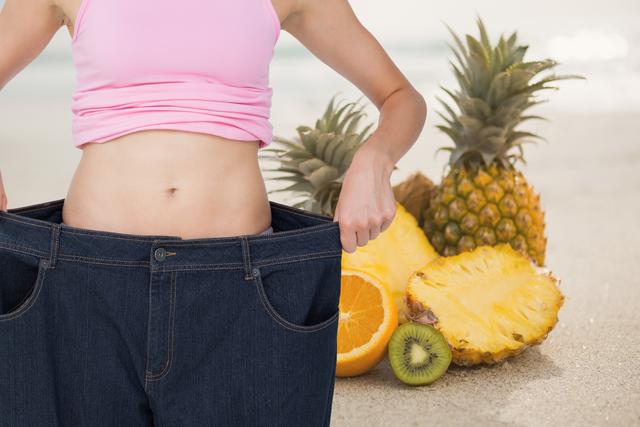 Digital composite of Midsection of woman in loose jeans by pineapples representing weight loss
