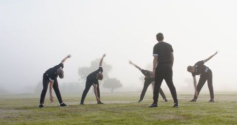 Group of Athletes Stretching in Morning Fog with Coach