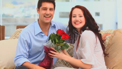 Man Presenting Roses to Smiling Partner on Couch