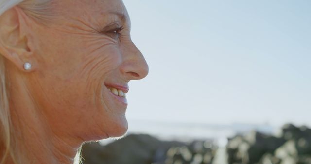 Older woman smiling outdoors with coastal rocks in background - Download Free Stock Images Pikwizard.com