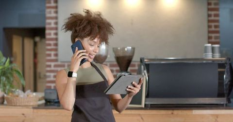 African american barista talking on phone while using tablet in cozy coffee shop
