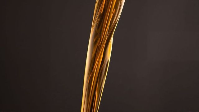 Pouring amber liquid stream with glossy highlights and viscous flow on dark background
