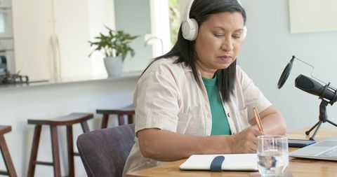 Midlife woman recording podcast while taking notes at minimalist home office