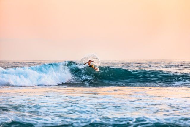 Surfer riding powerful ocean wave during golden sunset, showcasing skills and athleticism. Ideal for promoting surfing culture, beach vacations, water sports events, adventure photography, and healthy lifestyle content.