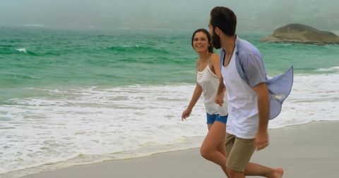 Joyful Couple Running Hand in Hand on Ocean Shoreline