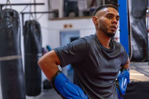 Focused boxer pausing in gym ring with blue gloves showing determination and conditioning