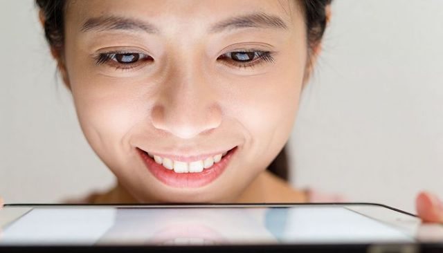 Smiling asian woman holding tablet below chin reflecting face closeup lifestyle