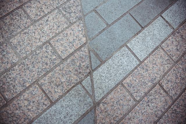 This image shows a close-up view of a paving stone road with a geometric pattern. The stones are arranged in a mix of grey and brown tones, creating an intricate design. This background is ideal for use in architectural presentations, urban planning projects, or as a texture in graphic design work.