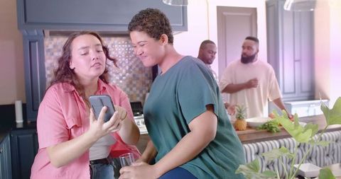 Friends gathering in modern kitchen sharing smartphone moment and casual conversation