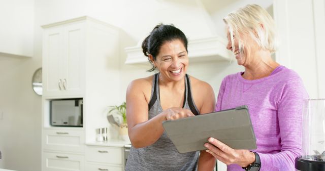 Two Mature Women Laughing and Using Digital Tablet in Kitchen - Download Free Stock Images Pikwizard.com