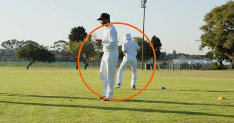 Cricket players practicing fielding drills on suburban outfield holding red ball and cones
