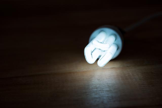 This image shows a close-up of a glowing bulb placed on a wooden table, highlighting its bright light and energy-efficient design. Ideal for use in articles or advertisements about energy-saving lighting solutions, home decor, modern interior design, or eco-friendly products.