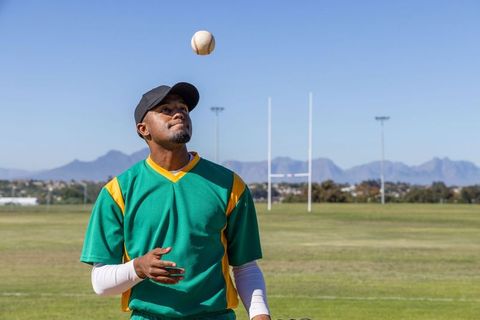 African american baseball player tossing ball on practice field with mountain backdrop