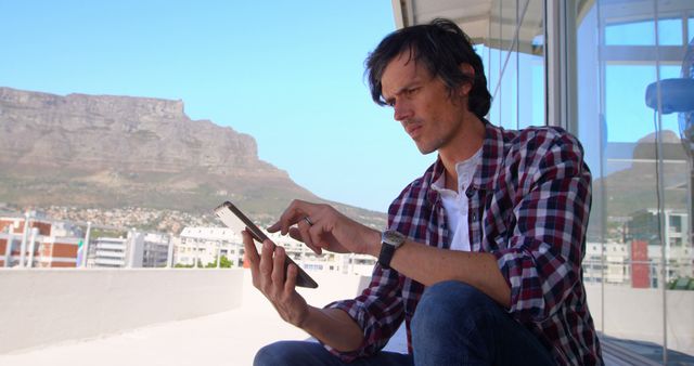 Man Sitting on Balcony Using Tablet with Mountain View Background - Download Free Stock Images Pikwizard.com