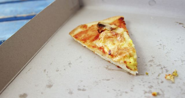 Single slice of pizza remaining in a plain cardboard box, cheesy with light toppings. Ideal for themes related to takeaway food, casual dining, food delivery, wastefulness, or concluding a meal.