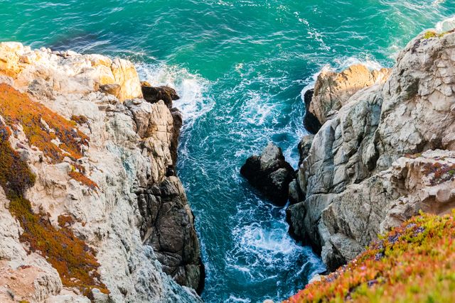 Beautiful aerial view capturing rocky coastal cliffs meeting turquoise sea below. Waves crashing against the rocks create a dynamic and natural seascape. The vibrant colors and texture of the cliffs contribute to the stunning scenery, ideal for travel brochures, nature websites, and beach-inspired designs.