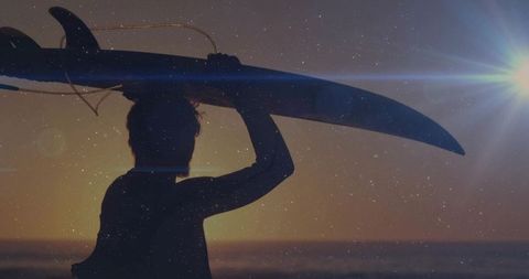 Male surfer walking toward ocean carrying longboard at golden hour silhouette
