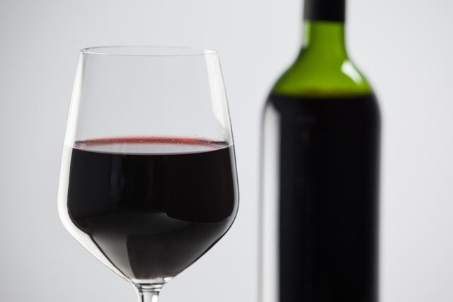 Bottle and a glass of red wine against white background